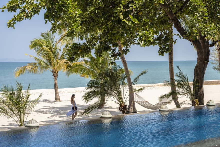 View of a woman walking on a tropical beach from a private pool