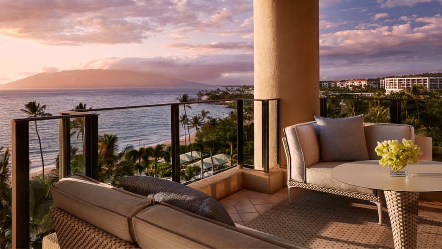 Luxury balcony with cushioned seating and table overlooking a tropical beach and ocean at sunset