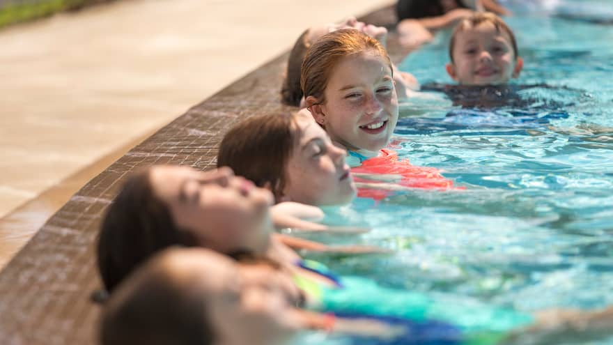 Close-up of five children side-by-side with heads above water in swimming pool