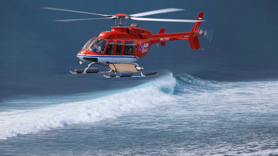 A helicopter hovers over the water for a guest to go helisurfing