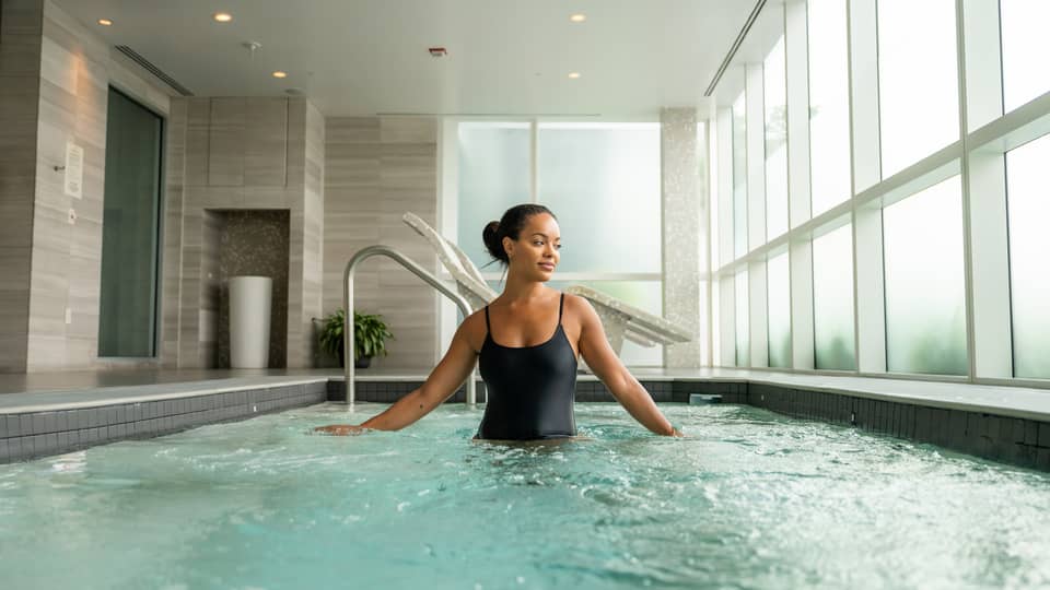 Guest wearing a swimsuit and standing in the pool in a room with floor-to-ceiling windows.