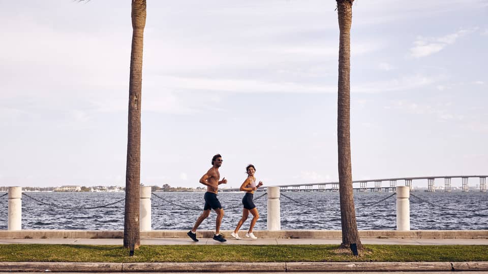 Man and woman running on sidewalk next to water