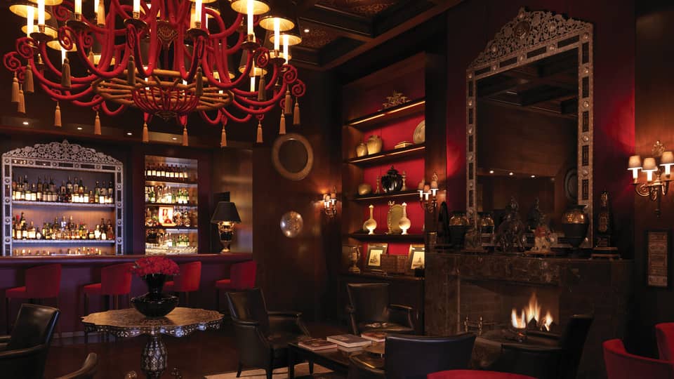 Bar interior with dark wood, red chandelier, shelf and velvet bar stools, arabesque ceiling, fireplace