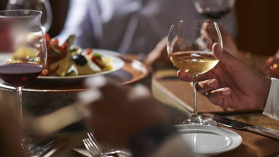 Close-up of hand holding wine glass by dinner plate on table