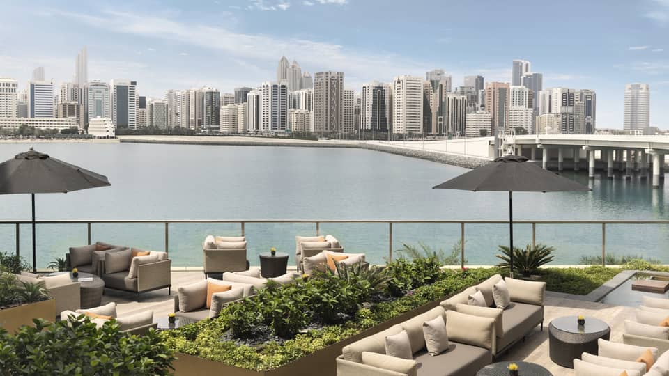 Outdoor sofas, umbrellas and planters on patio overlooking water, city
