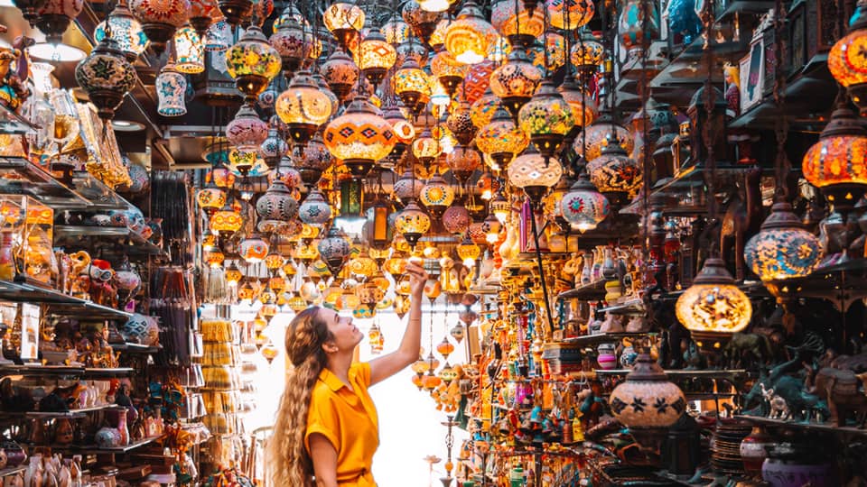 A woman in a yellow dress stands in the centre of a market under a series of bright lamps.
