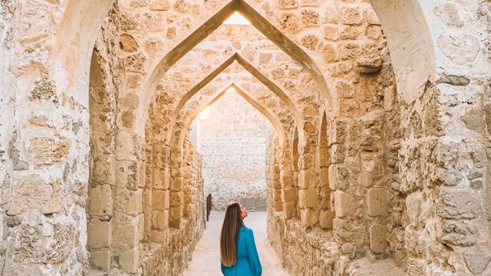 A woman stands underneath a stone pathway.