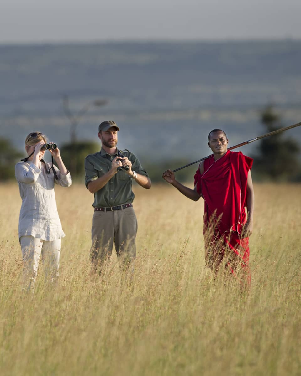 Couple takes photos on walking safari through tall grass with guides