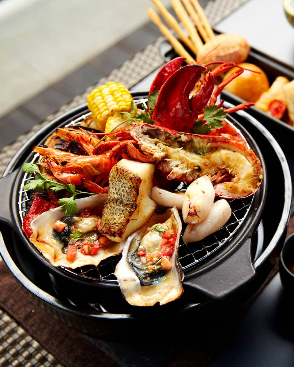 Grilled fish, oysters, lobster, crab on grill plate next to white wine, garnishes