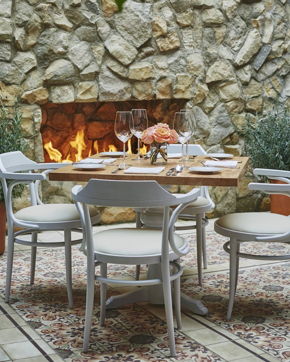 Close-up of white chairs and dining table set with wine glasses, flowers, in front of brick fireplace