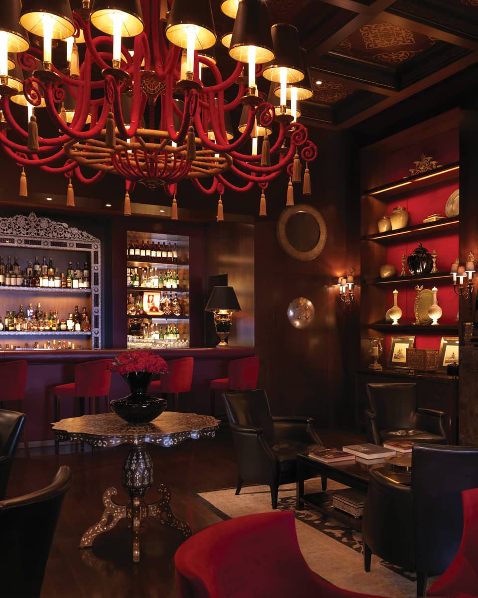 Bar interior with dark wood, red chandelier, shelf and velvet bar stools, arabesque ceiling, fireplace