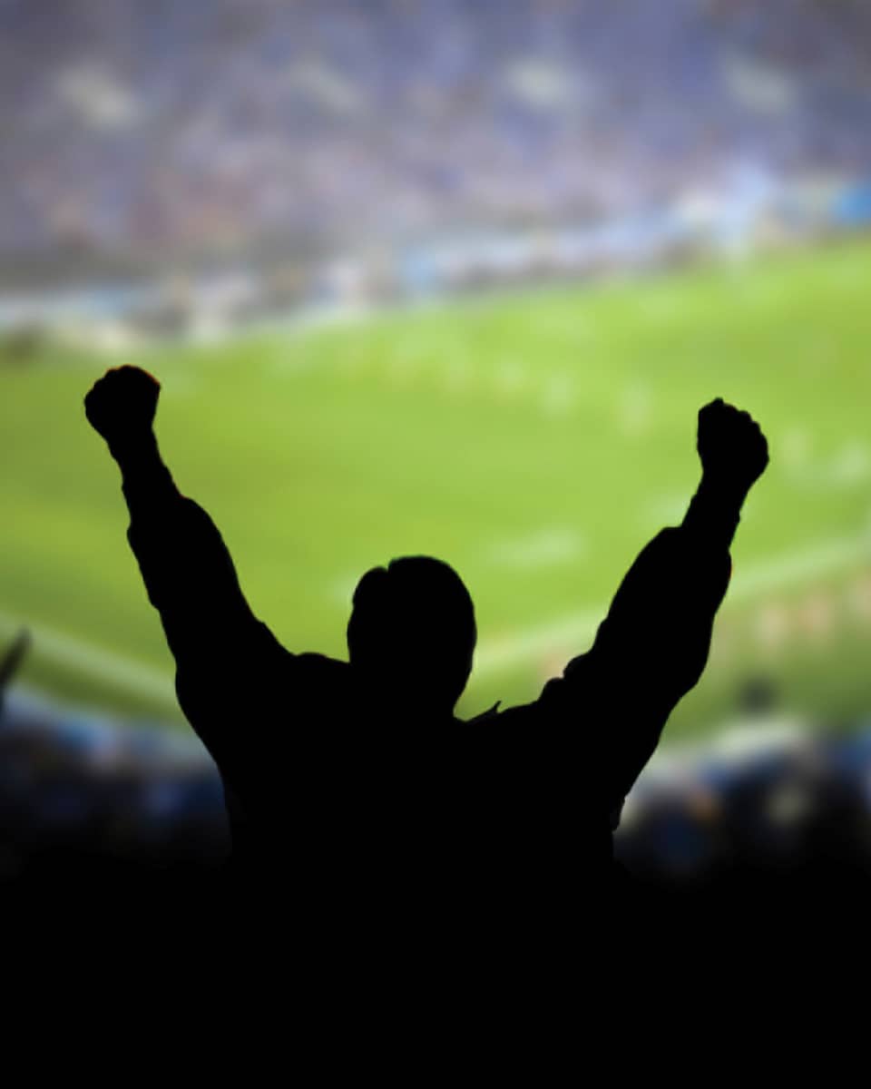 A silhouette of a person cheering at a football stadium.