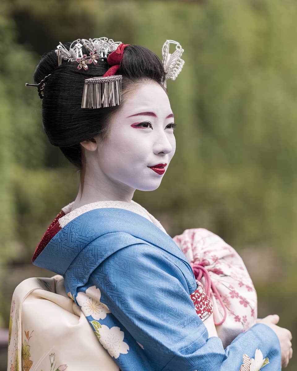 Close-up of a maiko wearing traditional makeup and a blue kimono with hair ornaments