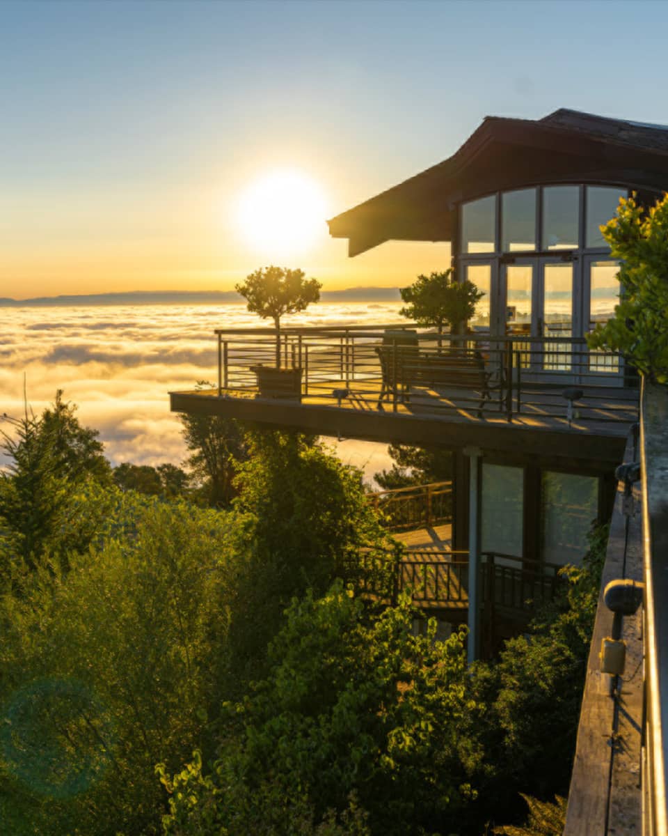 Two-story house surrounded by trees and the ocean with a sunrise.