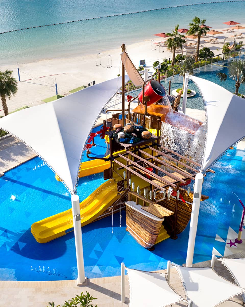 A large orange waterslide built into a faux pirate ship descending into a crystal blue pool of water.