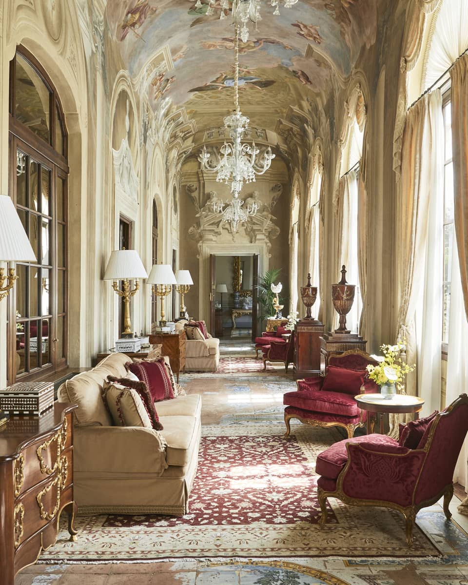 Grand, arched hallway with frescoed ceiling and chandelier, lounge seating and ruby-red arm chairs, in the Royal Suite at Four Seasons Hotel Florence