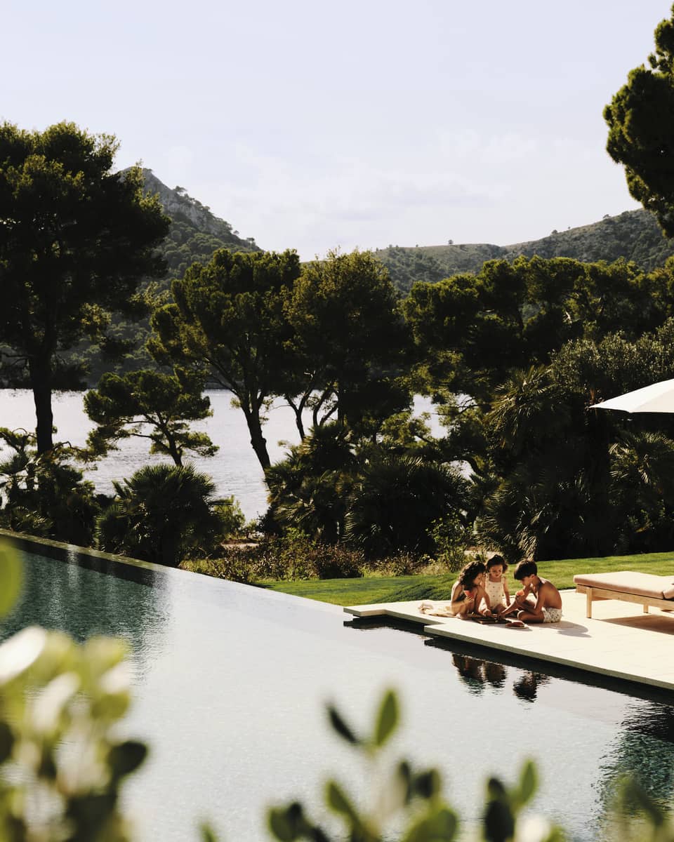 young children play on pool deck next to large resort pool, surrounded by push pine trees