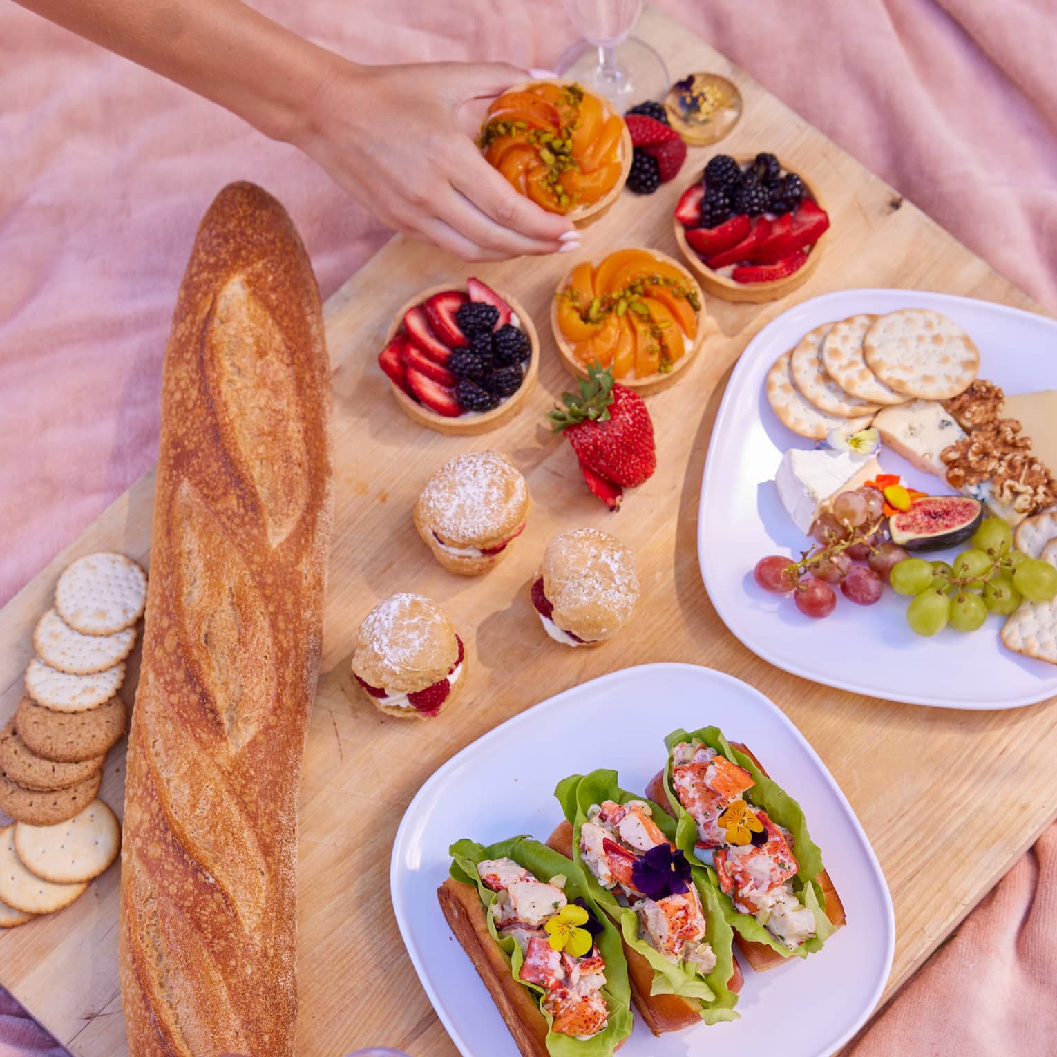 Plates of food and bowls of fruit on a picnic blanket
